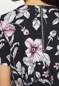 Černý květinový top s velkými růžovými a bílými květy a zelenými listy, doplněný stříbrným zipem na zadní straně. Hladká textilie.