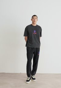 Gray cotton t-shirt with a round neckline and front graphic, paired with matching gray sweatpants. Black sneakers with white soles.