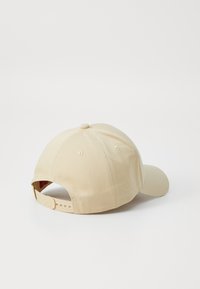 Beige baseball cap made of cotton with a slight texture. Features a curved brim and adjustable strap at the back with embossed logo.