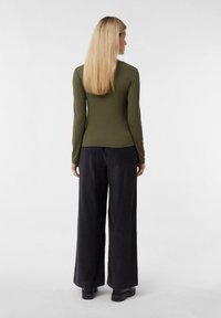 Długa bluzka w kolorze oliwkowej zieleni o dopasowanym kroju, zestawiona z luźnymi, czarnymi spodniami o szerokich nogawkach. Gładka faktura i minimalistyczne detale.