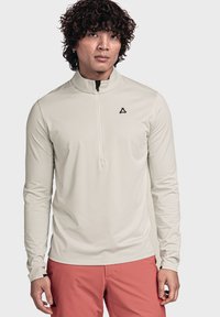 Helle beige Langarmbluse mit einem Halbreißverschlusskragen, aus einem glatten, dehnbaren Stoff; verfügt über ein kleines Logo auf der Brust.