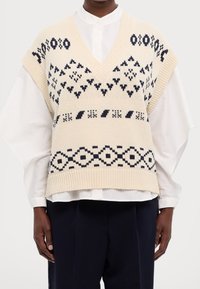 Pull sans manches tricoté en crème avec des motifs géométriques bleu marine, doté d'un col en V, d'un ourlet côtelé et d'emmanchures tombantes.