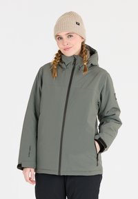 Grüne wasserdichte Jacke mit Reißverschluss, verstellbare Kapuze und zwei seitlichen Taschen. Getragen mit einer beigen gestrickten Mütze. Glatte Textur.
