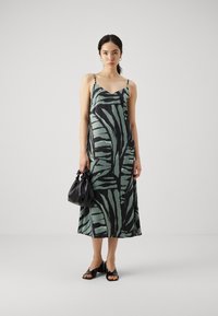 Satin midi kleita ar zaļo un melno lapu rakstu, regulējamām spaghetti siksnām, V formas izgriezumu, pārī ar melnu somu un atvērtu purngalu zābakiem.