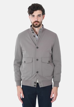 Giacca leggera grigia con colletto alto, dotata di quattro tasche frontali e chiusure a bottone, realizzata in tessuto morbido. Polsini elastici sulle maniche.