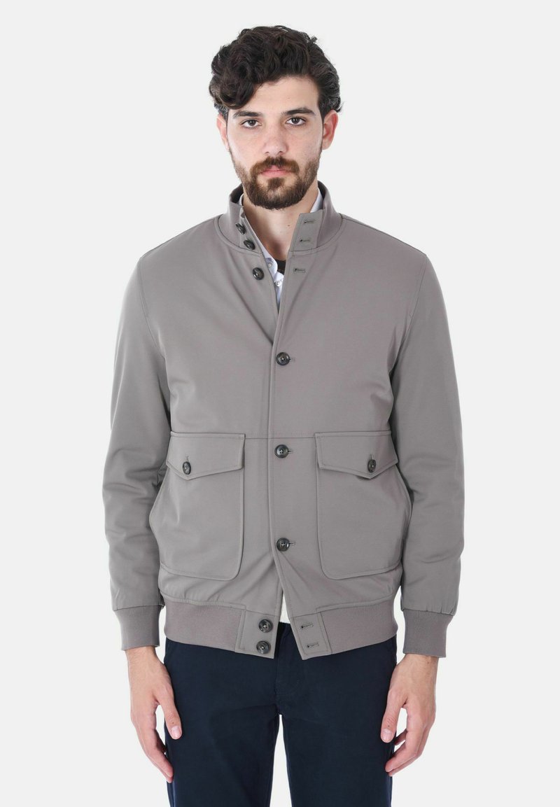 Giacca leggera grigia con colletto alto, dotata di quattro tasche frontali e chiusure a bottone, realizzata in tessuto morbido. Polsini elastici sulle maniche.