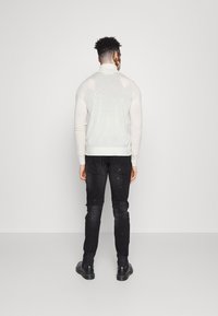 Suéter ajustado color crema con cuello alto, combinado con jeans negros de corte slim que presentan detalles desgastados. Botines negros completan el look.