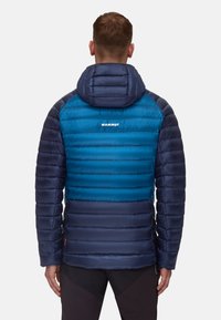 Doppelt gefütterte Jacke in Dunkelblau und Türkis mit Kapuze, vertikalen Steppnähten und einem Logo im oberen Rückenbereich, aus leichtem Material gefertigt.