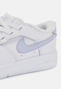 Bela športna obutev iz usnja z zračnimi modrimi detajli, okrogla konica, ravni vezalke in teksturiran gumijast podplat z oznako "NIKE".