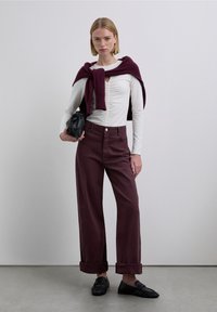 Pantalones anchos color burdeos con pliegues en el frente, top blanco de manga larga, bufanda oscura colgada, bolso negro y zapatos planos texturizados. Diseño minimalista.