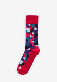 Chaussettes multicolores avec un motif géométrique audacieux, dotées d'un bord et d'un orteil rouges, fabriquées à partir d'un tissu doux et extensible. Le motif comprend des courbes et des blocs.