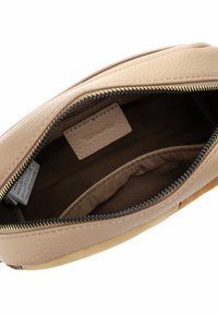Innenraum einer hellbeigen Ledertasche mit braunem Stofffutter, ausgestattet mit einem Reißverschluss und einer Einschubtasche. Ein Etikett ist sichtbar.