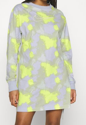Pitkähihainen tie-dye-mekko pastellinvioletin, harmaan ja neonkeltaisen sävyissä, jossa on tikattu Nike-logo rinnassa, päällä henkilö valkoista taustaa vasten.