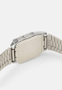 Montre en acier inoxydable argenté avec un boîtier octogonal, deux boutons-poussoirs sur le côté et un bracelet en métal texturé. Détails gravés à l'arrière.