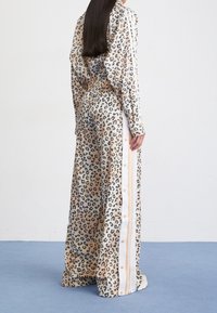 Leopardmönstrad jumpsuit i beige och svart med långa ärmar, midjeresår och kontrasterande vita sidsrevar med knappar.