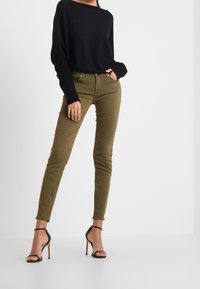 Suéter negro de gran tamaño, pantalones ajustados verde oliva y sandalias de tacón alto negro con tiras. Texturas suaves, corte a medida y diseño sencillo.