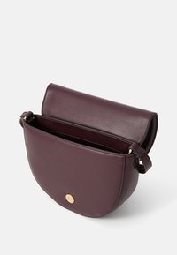 Borsa a tracolla in pelle bordeaux con una forma arrotondata, chiusura a pattina e accessori in tono oro. L'interno presenta un ampio scomparto.