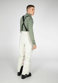 Witte skibroek met verstelbare zwarte bretels, gecombineerd met een groen shirt met lange mouwen. De broek heeft een relaxte pasvorm en heeft een lichte glans.