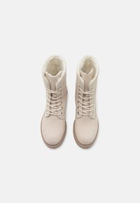 Botines de ante beige con forro de pelo sintético, puntera redonda y parte superior con cordones. Suela de goma con acentos de costura.
