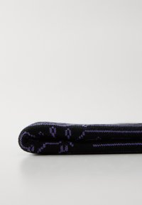Zwart gebreid kledingstuk met een opgerolde rand, voorzien van een paars geometrisch patroon en een gladde textuur. Zichtbare stiksels langs de randen.