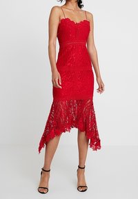 Robe en dentelle rouge avec bretelles spaghetti, corsage ajusté et ourlet en scallop. Présente des motifs floraux et un design asymétrique.