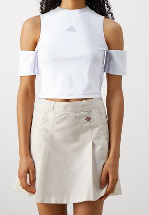 Weißes Crop-Top mit angeschnittenen Schultern und beigefarbener A-Linien-Rock mit Bund und Dickies-Logoaufnäher auf der Vorderseite.