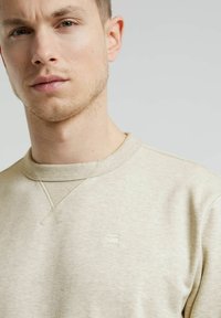 Felpa beige a collo rotondo con una sottile trama, caratterizzata da un piccolo logo impresso sul petto e un collo a costine.