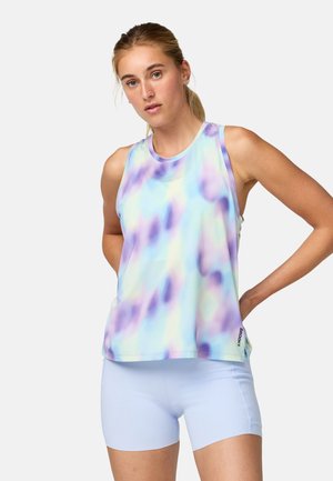 Jeune femme aux cheveux blonds attachés en queue de cheval, portant un haut sans manches tie-dye pastel bleu et violet et un short ajusté bleu clair.