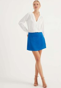 Vit blus med V-hals och rynkade axlar, matcherad med en klarblå A-linjeformad kjol. Lätt tyg, mittlängd upp till låren, slät textur.