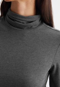 Grauer, langärmeliger Rollkragenpullover aus weichem Stoff, mit umgeschlagenem Kragen und glatter Textur, klaren Linien und minimalistischem Design.