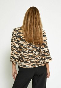 Top stampato con motivo a strisce di tigre beige, marrone e nero. Presenta maniche a tre quarti e una vestibilità comoda.