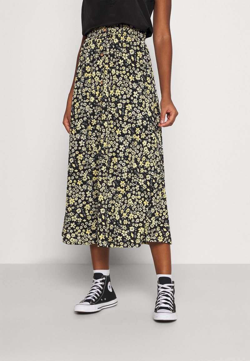 Gonna midi floreale nera con fiori gialli e bianchi, dotata di vita elasticizzata e dettagli con bottoni, abbinata a sneakers nere alte.