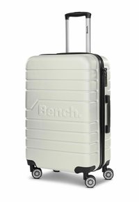 Valigia rigida bianca con superficie textured, cerniera nera, manico telescopico e quattro ruote piroettanti. Presenta un accento con il logo "Bench.".