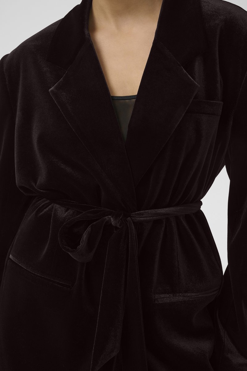 Schwarzer Samtmantel mit Kragen, gestaltet mit einem taillierten Design, vorderen Taschen und glatter Textur. Verfügt über ein satinartiges Finish und eleganten Fall.