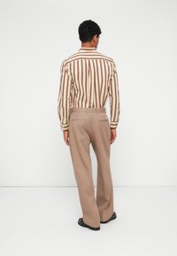 Svītraina garām piedurknēm krekls bēšā un brūnā krāsā, apvienots ar bēšām biksēm. Krekls ar vertikālām svītrām, pieguļošiem aprocēm; bikses ir platām kājām.