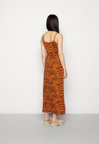 Robe maxi à motif rayures de tigre orange et marron, corsage ajusté, bretelles réglables, tissu lisse, portée avec des chaussures à plateforme de couleur claire.