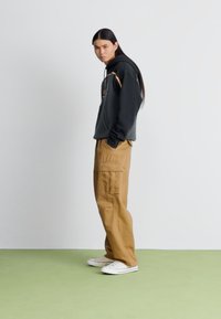 Black hoodie with graphic design, paired with khaki cargo pants featuring side pockets. Worn with white sneakers on a green floor.