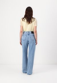 Top jaune clair avec des manches transparentes associé à un jean large taille haute bleu clair, avec une ceinture noire et deux poches arrière.