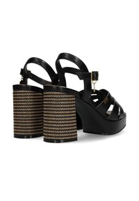 Černé kožené sandály na podpatku mají zakřivenou platformu a strukturovaný blokový podpatek s tkaným zlatým a černým vzorem, nastavitelné zapínání kolem kotníku.