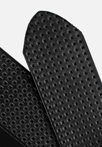 Plantillas de zapatos de goma negra con superficie texturizada que presenta pequeños patrones triangulares para mejorar el agarre y la comodidad.