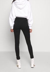 Mustat kapeat farkut viidellä taskulla, korkealla vyötäröllä ja sileällä, joustavalla pinnalla. Yhdistetty valkoiseen huppariin ja valkoisiin nilkkureihin.