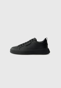 Schwarze Low-Top-Sneaker mit gerippter Plattformsohle, Schnürverschluss vorne und Zuglasche an der Ferse, auf einem schlichten hellen Hintergrund präsentiert.