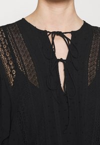 Abito nero con dettagli in pizzo elaborati, chiusura a lacci al collo, tessuto testurizzato con punti in rilievo e una vestibilità rilassata.