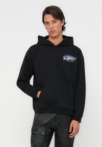Sweat-shirt à capuche noir en mélange de coton, avec une poche avant et un graphisme coloré sur la poitrine gauche. Texture lisse, coupe décontractée.