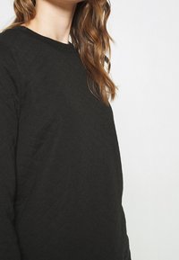 Sweat-shirt noir matelassé avec un col rond, présentant un motif texturé et une coupe décontractée. Fabriqué dans un matériau doux et léger.