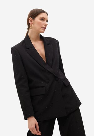 Blazer negro de doble botonadura con tela texturizada, acentos de puntos, solapas anchas y bolsillos delanteros, combinado con un escote en V profundo.