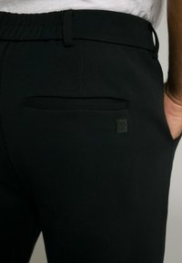 Schwarze Jogginghosen mit glatter Textur, ausgestattet mit einem elastischen Taillenbund und einer Gesäßtasche mit kleinem Logo.