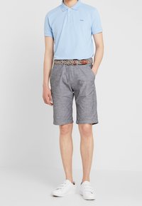 Polo bleu clair à manches courtes, short gris en tissu texturé, et ceinture tressée marron ; assortis à des baskets blanches.