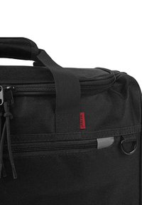 Bolsa de tela negra con un compartimento principal con cremallera, superficie texturizada, bolsillo lateral y una etiqueta roja. Cuenta con un asa resistente para llevarla.