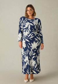 Námořnická květinová maxi šaty s dlouhými rukávy, zdobené bílými vzory listů. Hladká tkanina s mírně volným střihem. Hladké bílé boty.